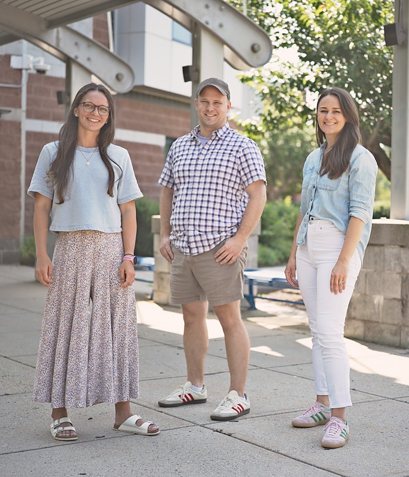 Gogy founders Sarah Bromley, Drew Hoover, and Aly Jenny standing together on a school walkway.